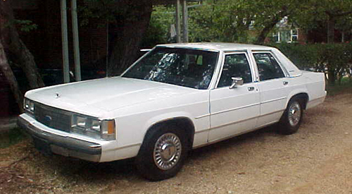 White Ford Crown Victoria four-door sedan front three-quarter view on gravel drive