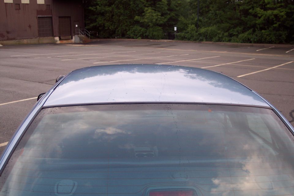 Rear and roof of a light blue sedan with reflections, parked in an empty lot.