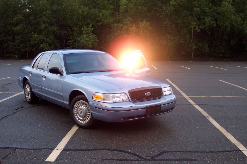 Light blue 2001 Ford Crown Victoria sedan with driver's door open and sun flare.