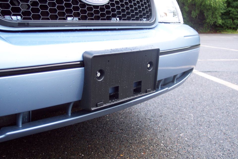 Front bumper of a light blue vehicle with a black license plate bracket.