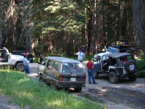 2005 Jeep Wrangler - Several off-road vehicles, including a Jeep Wrangler and a Toyota van, are parked on a dirt road in a forest. People are standing around th…
