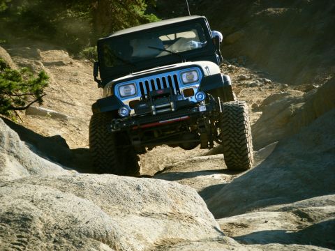 2005 Jeep Wrangler - A dark-colored Jeep Wrangler is navigating a rocky, off-road trail with large tires gripping the terrain. The front of the vehicle is angle…