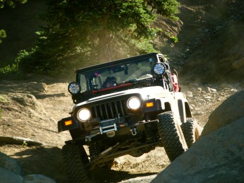 2005 Jeep Wrangler - A dark colored Jeep Wrangler is navigating a rocky, off-road trail with steep inclines and large boulders. The vehicle is angled upwards, w…