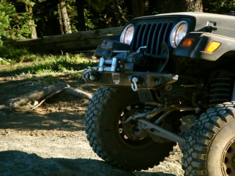 2005 Jeep Wrangler - The front quarter of a dark colored Jeep Wrangler is shown parked on a dirt path in a wooded area. Visible modifications include a winch mo…