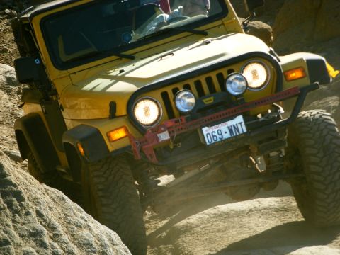 2005 Jeep Wrangler - A yellow Jeep Wrangler is shown from a 3/4 front angle, navigating a rocky, off-road trail. Visible modifications include a winch and a lic…