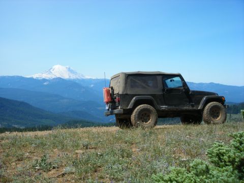 2005 Jeep Wrangler - A black Jeep Wrangler is parked on a grassy hillside with a snow-capped mountain range in the background under a clear blue sky. A red jerr…