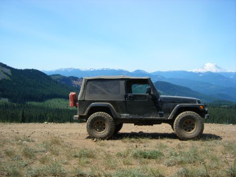 2005 Jeep Wrangler - A black Jeep Wrangler is parked on a dirt road overlooking a mountainous landscape with a snow-capped peak in the distance. A red jerry can…