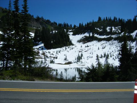 2005 Jeep Wrangler - A scenic view of a snow-covered mountain slope with scattered evergreen trees and a calm lake in the foreground, under a clear blue sky.