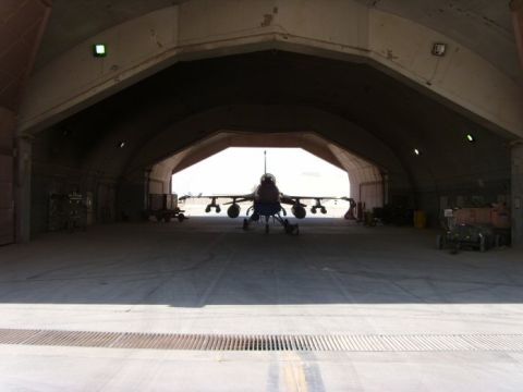 1978 Ford Bronco - A fighter jet is parked inside a large hangar. The opening of the hangar reveals a bright, sunny outdoor scene.