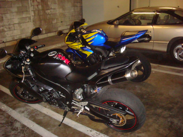 Black and blue/yellow sportbikes parked in a garage with a silver coupe.