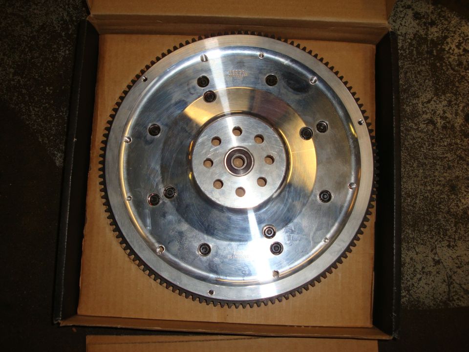Silver aftermarket flywheel with ring gear inside a cardboard box