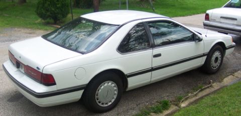 1991 Ford Crown Victoria LTD - A white 1989 Ford Thunderbird coupe is parked on a gravel surface next to another vehicle.