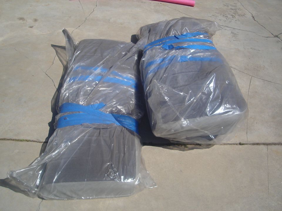 Two large items wrapped in plastic and secured with blue tape on concrete.
