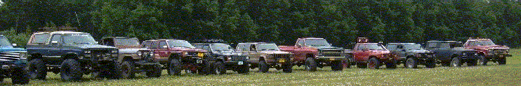 Row of lifted 4x4 trucks and SUVs parked on grass at an outdoor event