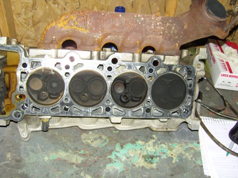 2007 Ford Mustang - Photograph of a cylinder head with valves and a rusted exhaust manifold on a workbench.