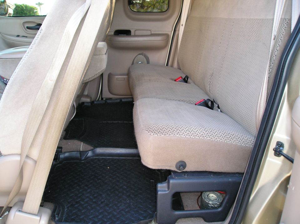 Interior of a pickup truck rear seat area with tan seats and black floor mats.