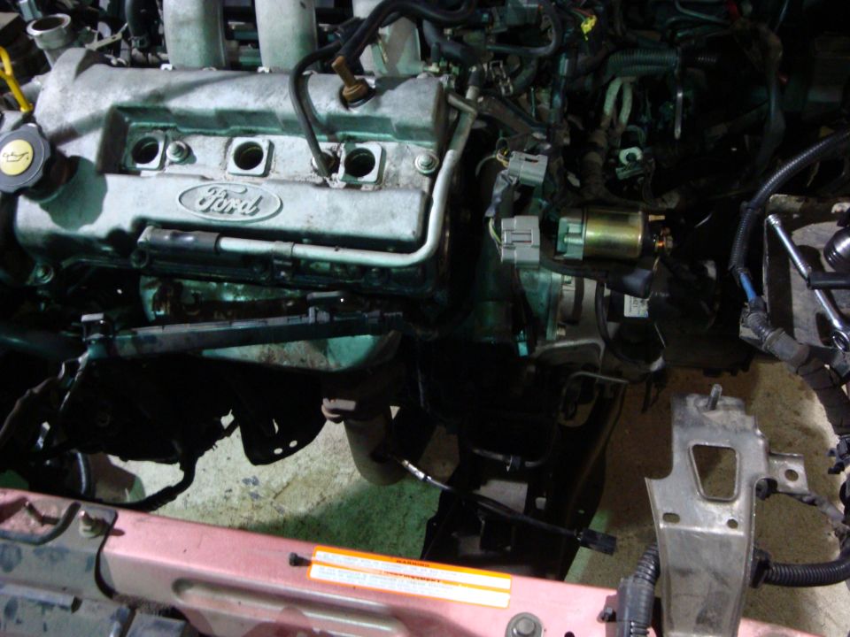 Ford engine with valve cover exposed during disassembly, pink radiator support in foreground