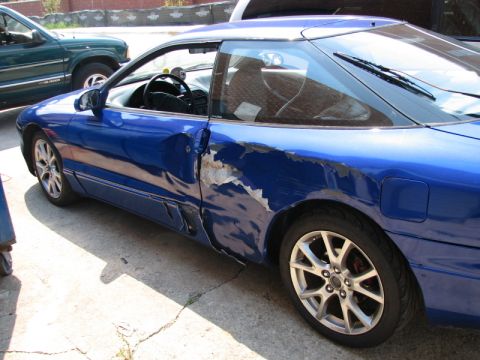 1993 Ford Probe - A blue 1993 Ford Probe shows significant damage to the driver's side door and rear quarter panel. The car is parked on a concrete surface n…