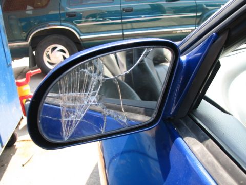1993 Ford Probe - A close-up of a cracked driver's side mirror on a blue car. The mirror reflects another vehicle and a red and yellow toy.