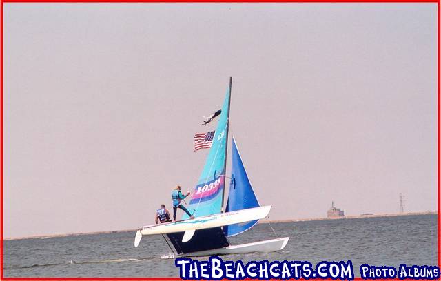 Catamaran sailboat with two people sailing on the water.