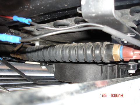 1979 Ford Bronco - A close-up view shows a black, ribbed rubber boot protecting a hose assembly with brass fittings and a red connector. Wires with blue conne…