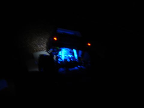 1996 Ford Bronco - Very dark nighttime photo of a vehicle showing blue underbody glow lighting and two red rear lights, surroundings mostly black.