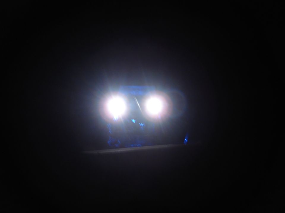 Illuminated headlights and blue lights on a vehicle at night.