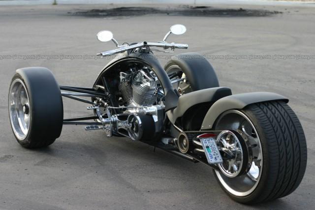 Custom V-twin trike with two front wheels and wide rear tire, rear three-quarter view.