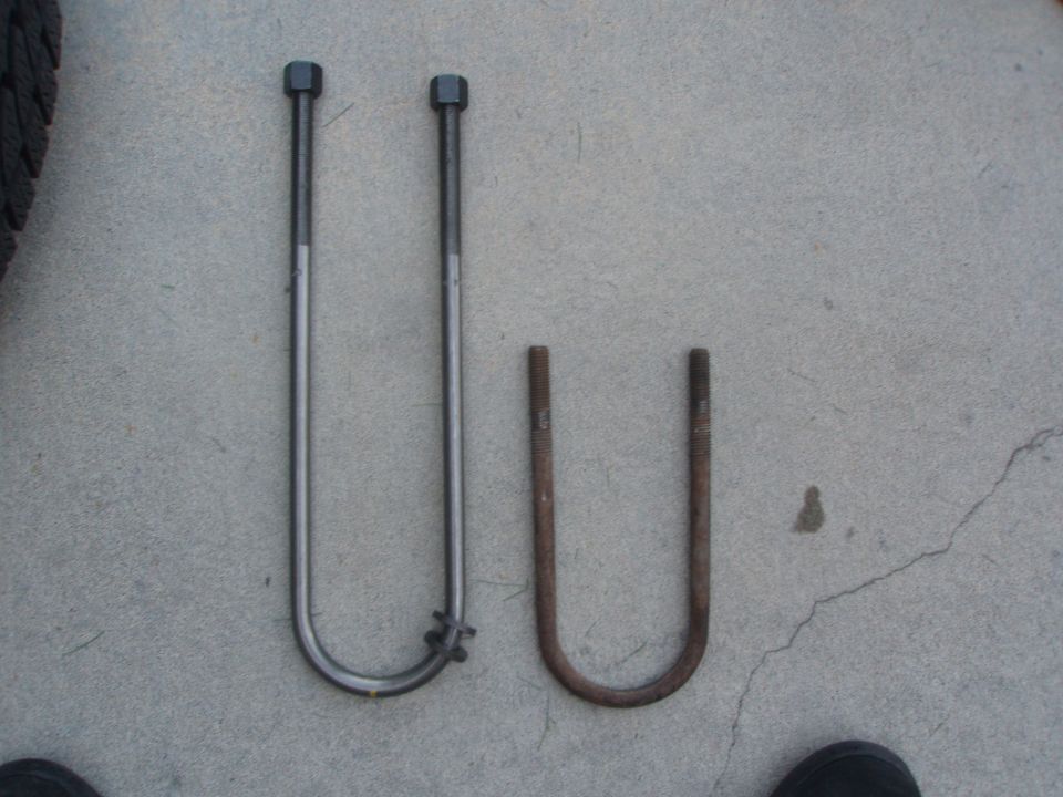 Two U-bolts on a concrete surface, one polished and longer, one rusted and shorter.