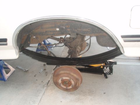 1987 Ford Bronco - The underside of a white vehicle, likely a Ford Bronco, showing the rear axle, leaf springs, and brake drum. A jack is supporting the leaf…