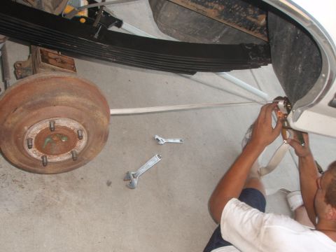 1987 Ford Bronco - A person works on the rear suspension of a vehicle, focusing on the leaf springs and brake drum. Tools like wrenches are laid out on the co…