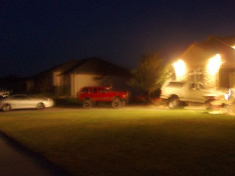 1987 Ford Bronco - A red SUV is parked in front of a house at night, with a silver sedan to its left and a white pickup truck to its right.