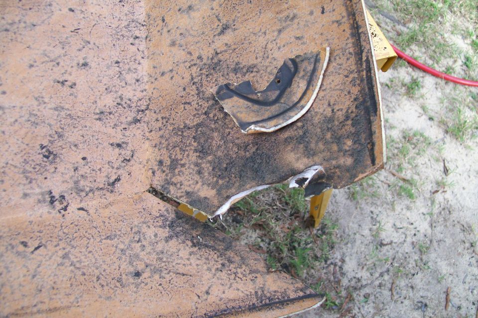 Damaged orange-brown vehicle panel with black streaks and a torn section.