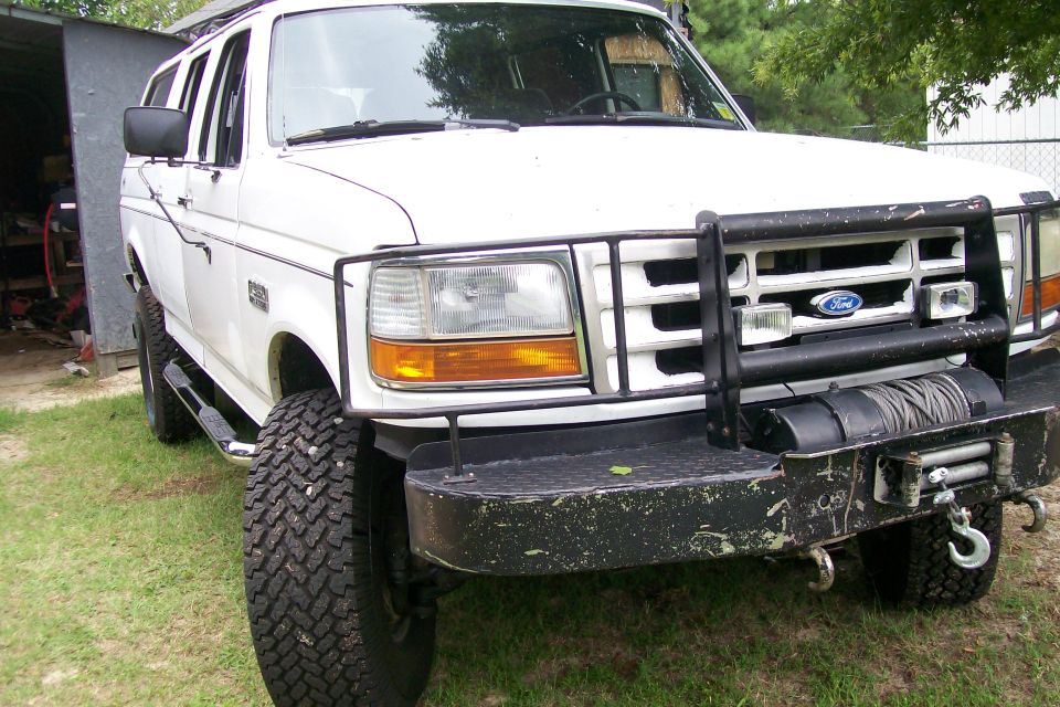 White Ford truck with black brush guard and winch, parked on grass.