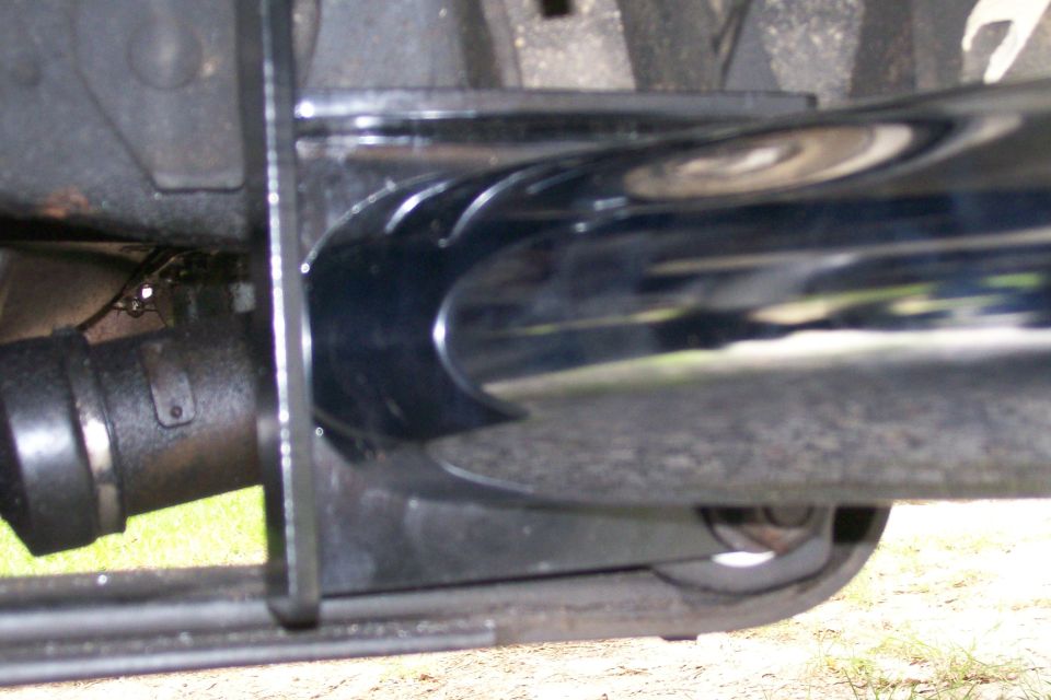 Chrome exhaust pipe with cutouts and black clamp under a vehicle.