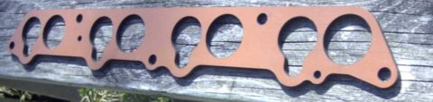 1997 Ford Taurus - A copper-colored gasket with multiple circular cutouts is laid across a weathered wooden surface. The gasket appears to be for an engine ma…