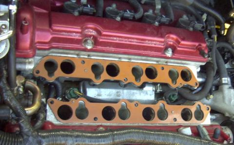 1997 Ford Taurus - A close-up view of the intake manifold gaskets on a red engine valve cover. The copper-colored gaskets have multiple circular openings for…