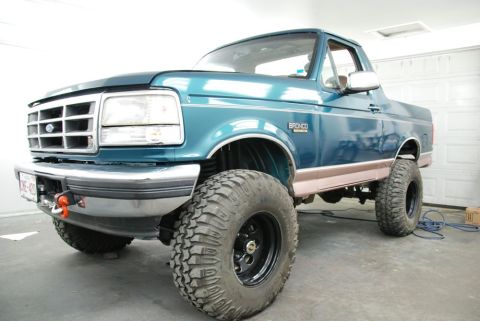 1996 Ford Bronco - Photograph of a teal lifted Ford Bronco parked in a garage, not a document.