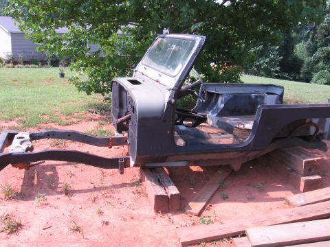 1980 Jeep CJ7 - A disassembled Jeep CJ7 body and frame are resting on wooden blocks in a sandy, grassy outdoor setting. The vehicle appears to be undergoin…