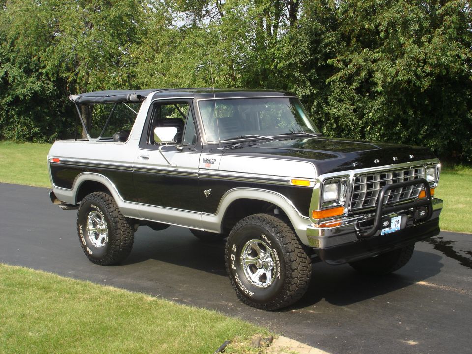 1979 Ford Bronco with black soft top, chrome wheels, and brush guard parked outdoors.