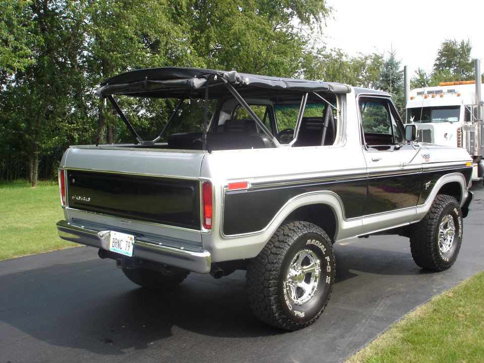 1979 Ford Bronco with soft top, silver and black, parked on driveway with semi-truck in background.