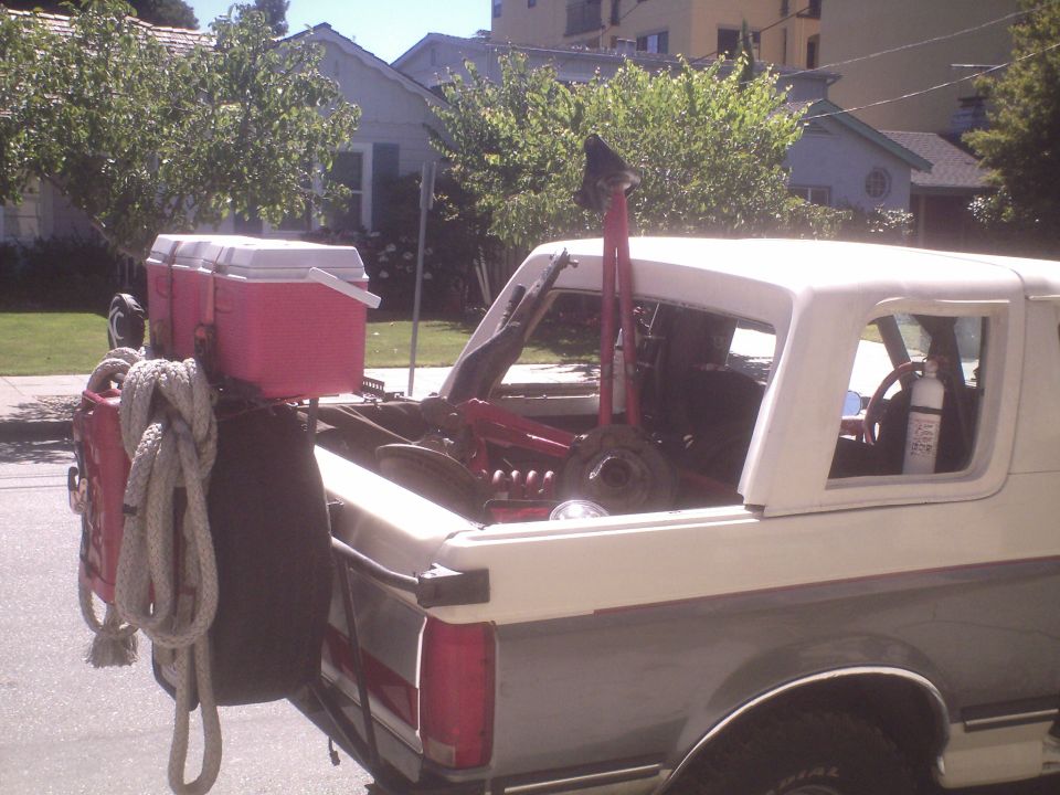 Rear view of a white and grey pickup truck bed loaded with coolers, rope, and equipment.