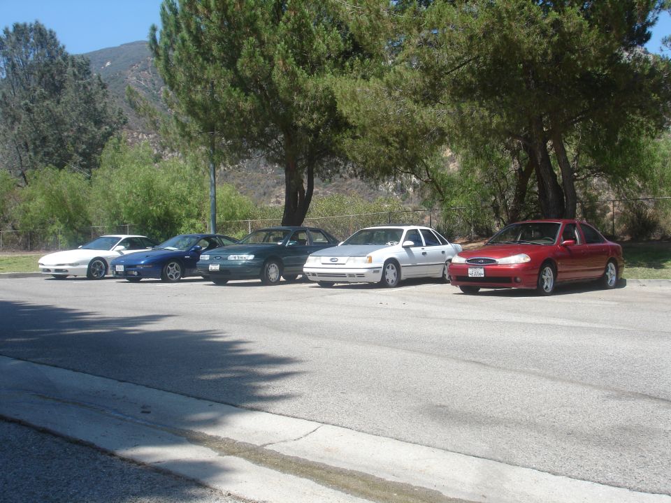 Five sedans parked in a row next to trees.