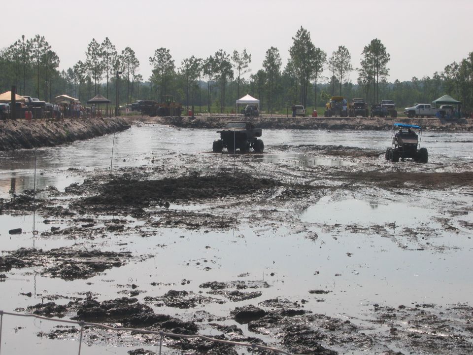 Lifted truck sitting in a flooded mud bog pit with spectators along the bank
