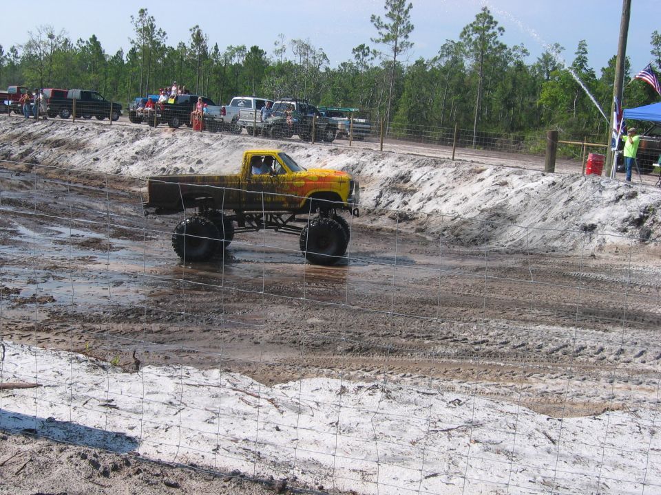 Yellow flamed lifted pickup on big tires running a mud pit at a mud bog event