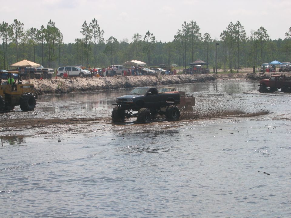 Dark blue lifted pickup on mud tires crossing a mud pit at a mud park