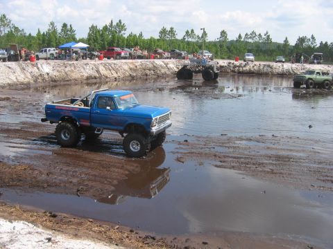 1992 Ford Bronco - A blue pickup truck navigates a muddy terrain with another vehicle visible in the distance.