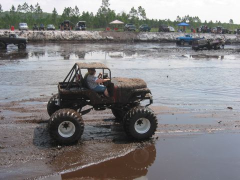 1992 Ford Bronco - Off-road vehicle with oversized tires parked on a wet surface, likely near water.