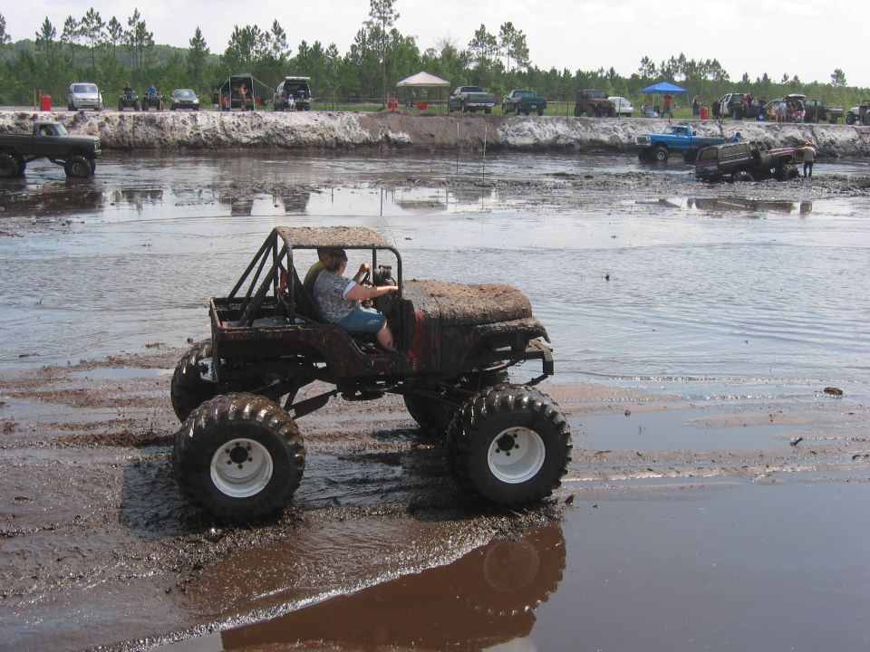 Modified off-road vehicle with large tires on wet ground, possibly a beach