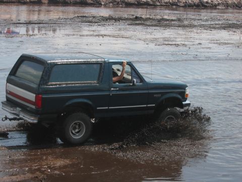 1992 Ford Bronco - A 1992 Ford Bronco navigates through a muddy off-road course, kicking up water and mud.